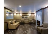 Small lounge with sofas and armchairs arranged around a corner fireplace and artwork under recessed ceiling lights.