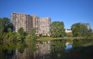 A multi-story senior living facility building named Parkshore Senior Campus is visible across a calm body of water, with trees and greenery surrounding the area and reflecting in the water.