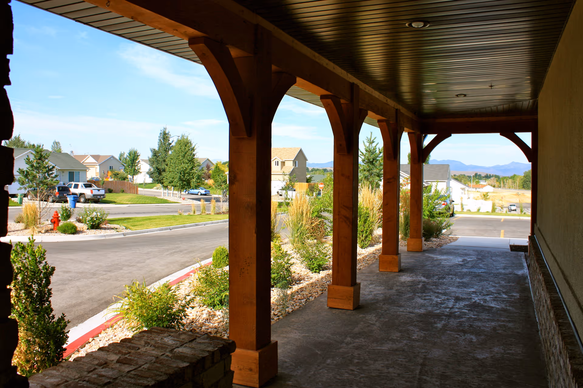 Covered wooden porch with columns overlooking a landscaped suburban street and distant houses and mountains.