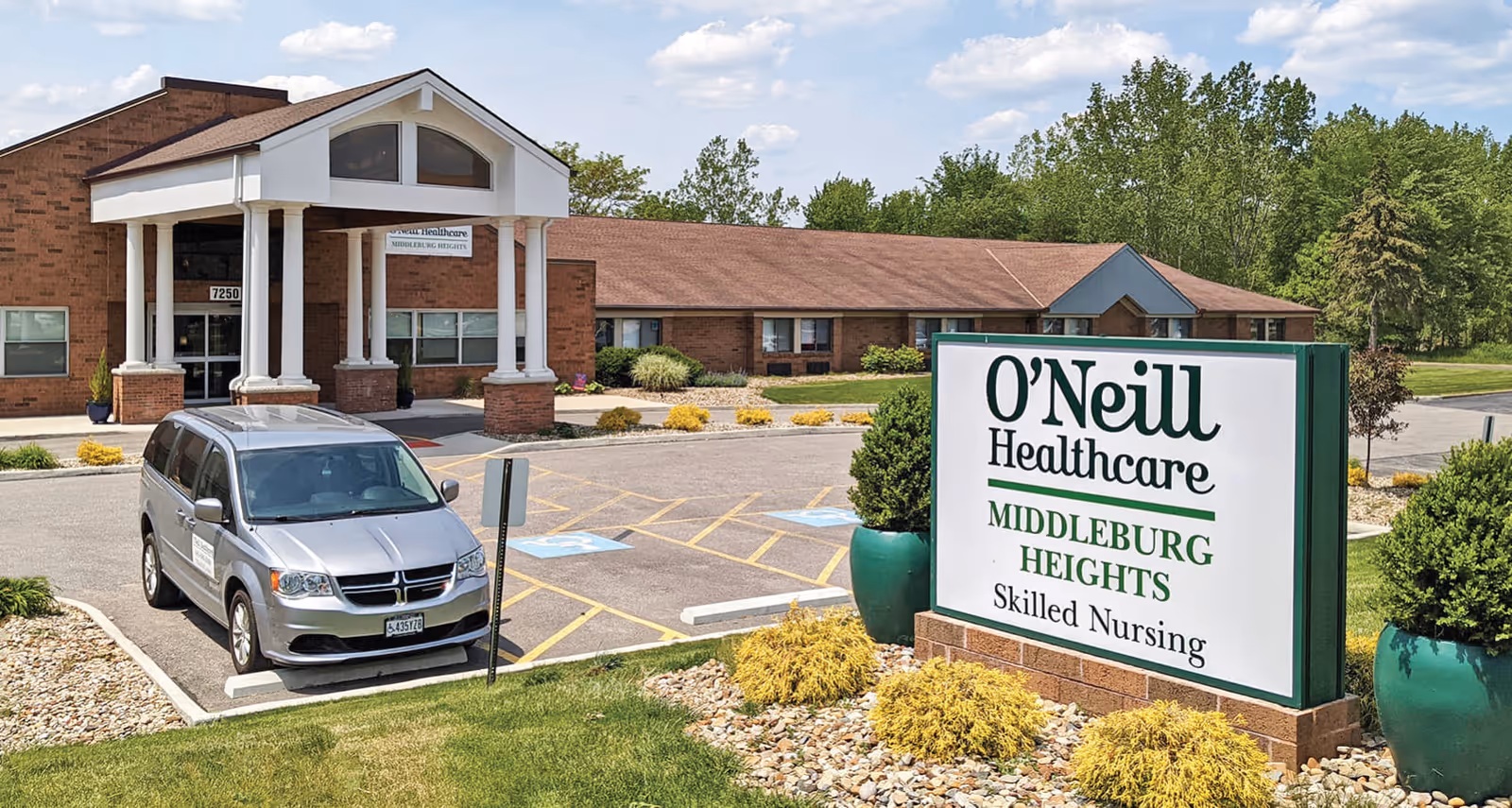 Exterior view of O'Neill Healthcare Middleburg Heights skilled nursing facility showing the main entrance with a covered portico, a parked silver van, a parking lot with handicap spaces, and a large sign with the facility's name surrounded by landscaping and greenery.