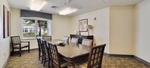 A rectangular dining table with chairs in a well-lit senior living dining room.