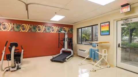 Interior fitness room with treadmill and exercise equipment in a senior living facility.