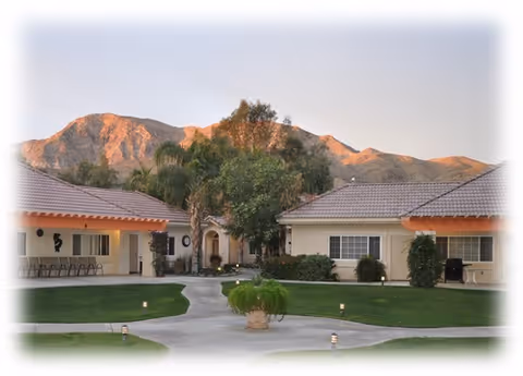 Courtyard of single-story buildings surrounding a manicured lawn and walkway with mountains in the background.