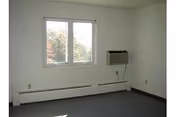 Empty carpeted room with a window, wall-mounted air conditioner and baseboard heater.