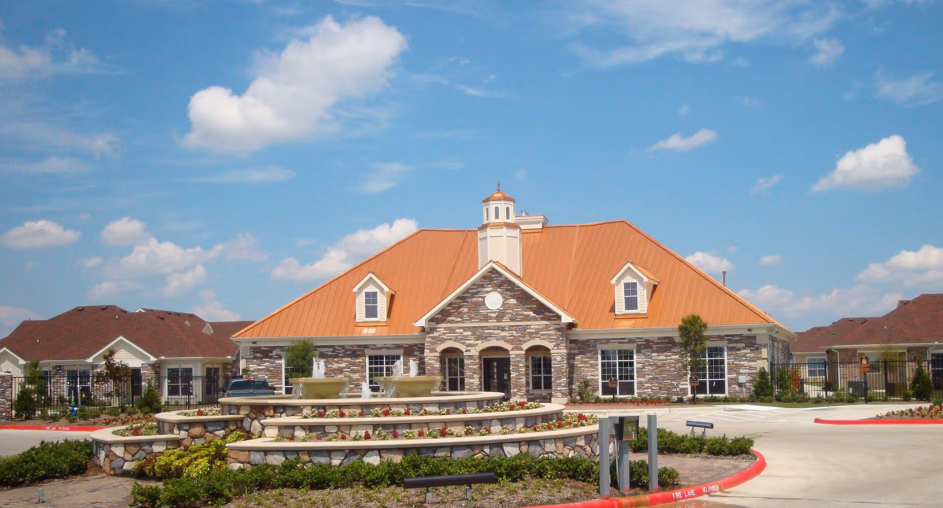 Exterior view of Attiva Pearland senior living facility with stone facade and fountain.