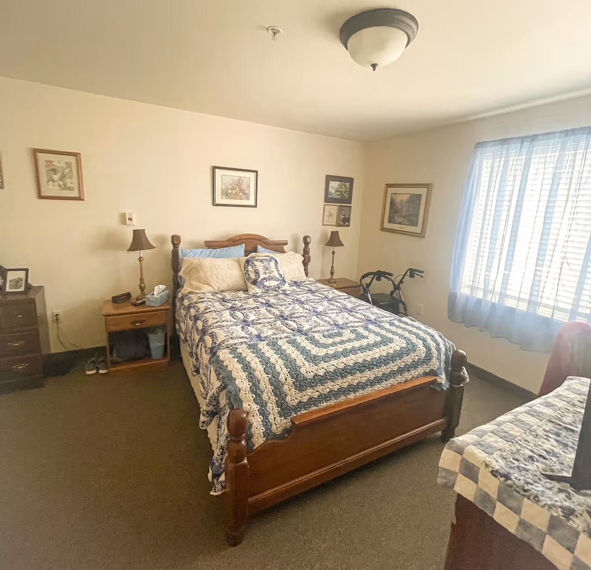 Cozy bedroom with a wooden bed, quilt, nightstands, lamps, and a walker by the window.