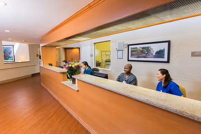 A reception/nurse's station inside a senior living facility with staff seated behind a long counter.