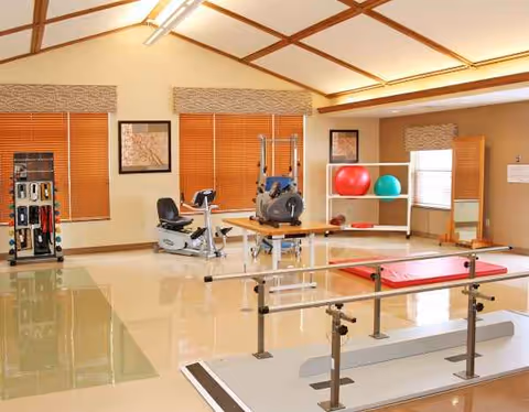 Interior rehab gym in a senior facility with exercise machines, balance bars, and therapy equipment.