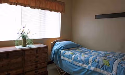 A small bedroom with a single bed, dresser, and a vase by the window.