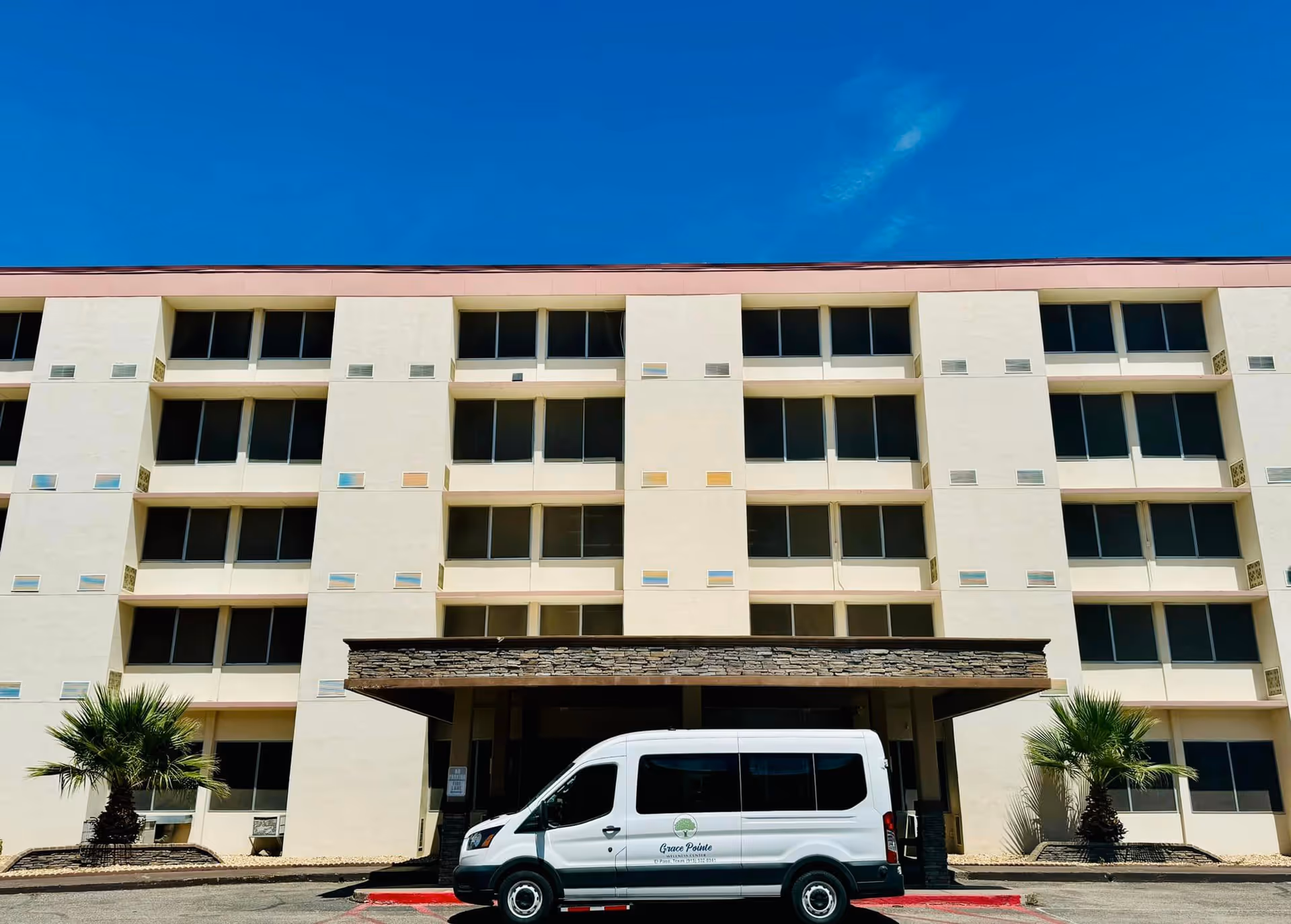 Front view of a multi-story senior living building with an entrance canopy and a white Grace Pointe shuttle van parked outside.