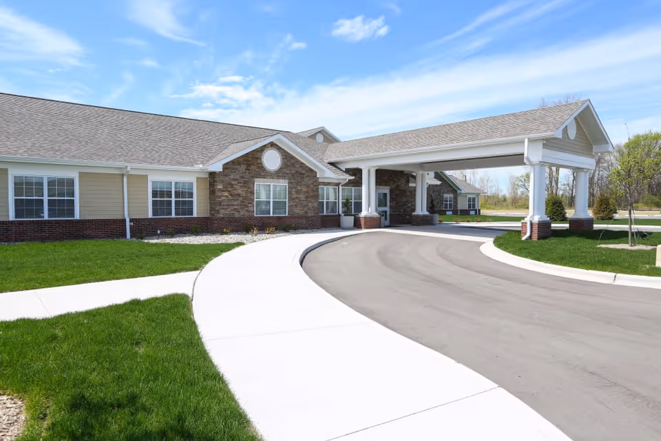 Front entrance of a single-story senior living building with a covered porte-cochere and a curved driveway.