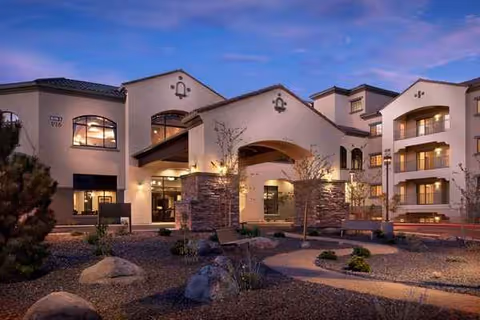 Exterior view of Alta Vista senior living facility, featuring arched entryway, stone columns, and desert landscaping.