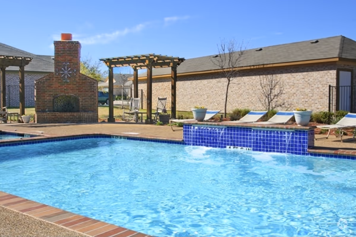 Outdoor swimming pool with blue-tiled spa edge, lounge chairs, pergola seating, and a brick outdoor fireplace.