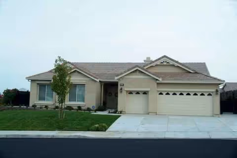 A beige single-story house with a two-car garage and a manicured lawn.