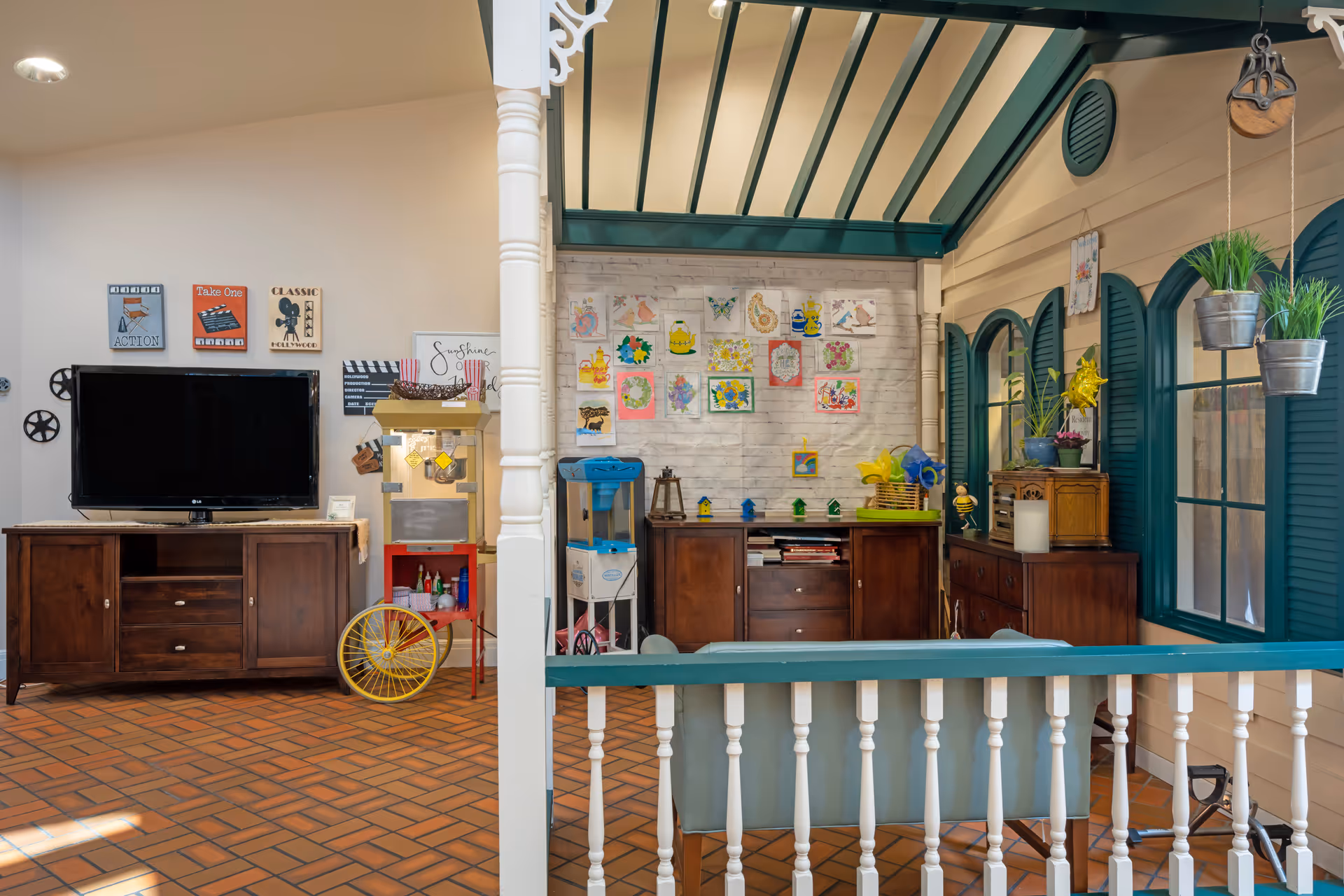 Bright communal activity room with a TV, cabinets, craft supplies and colorful artwork on the wall under a decorative indoor pergola.