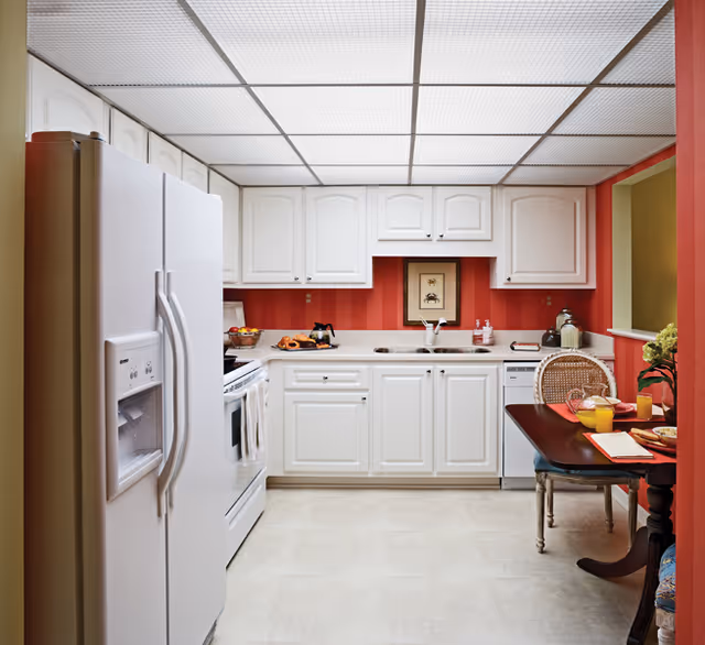 Small kitchen with white cabinets and appliances, red-striped walls, and a breakfast table.