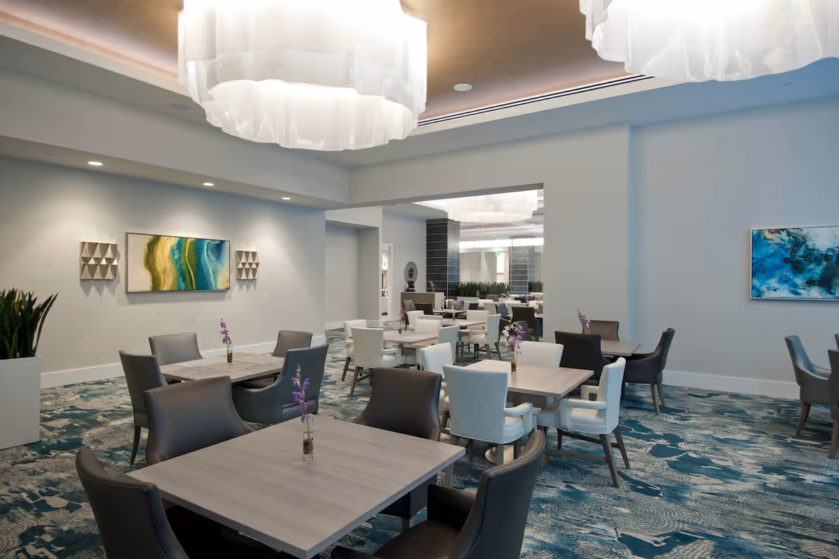 Spacious modern dining room with multiple tables and chairs, decorative pendant lights, artwork on the walls, and a patterned carpet.