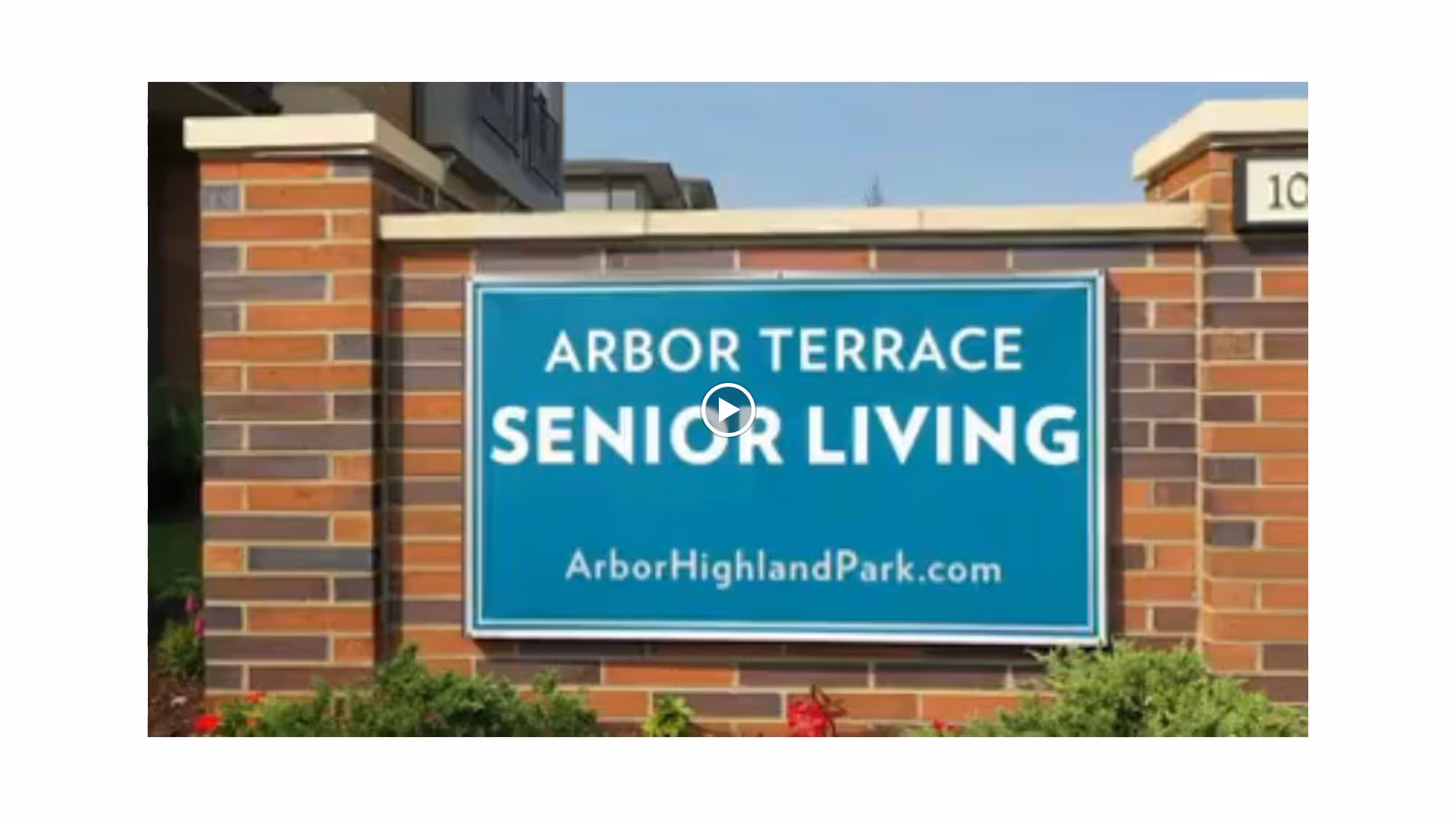 A brick signpost with a blue sign that reads 'Arbor Terrace Senior Living' and the website 'ArborHighlandPark.com' in front of a building under a clear sky.
