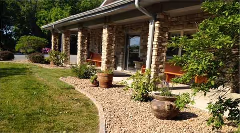 Exterior view of Carroll House with stone columns, benches, and potted plants along a gravel path.