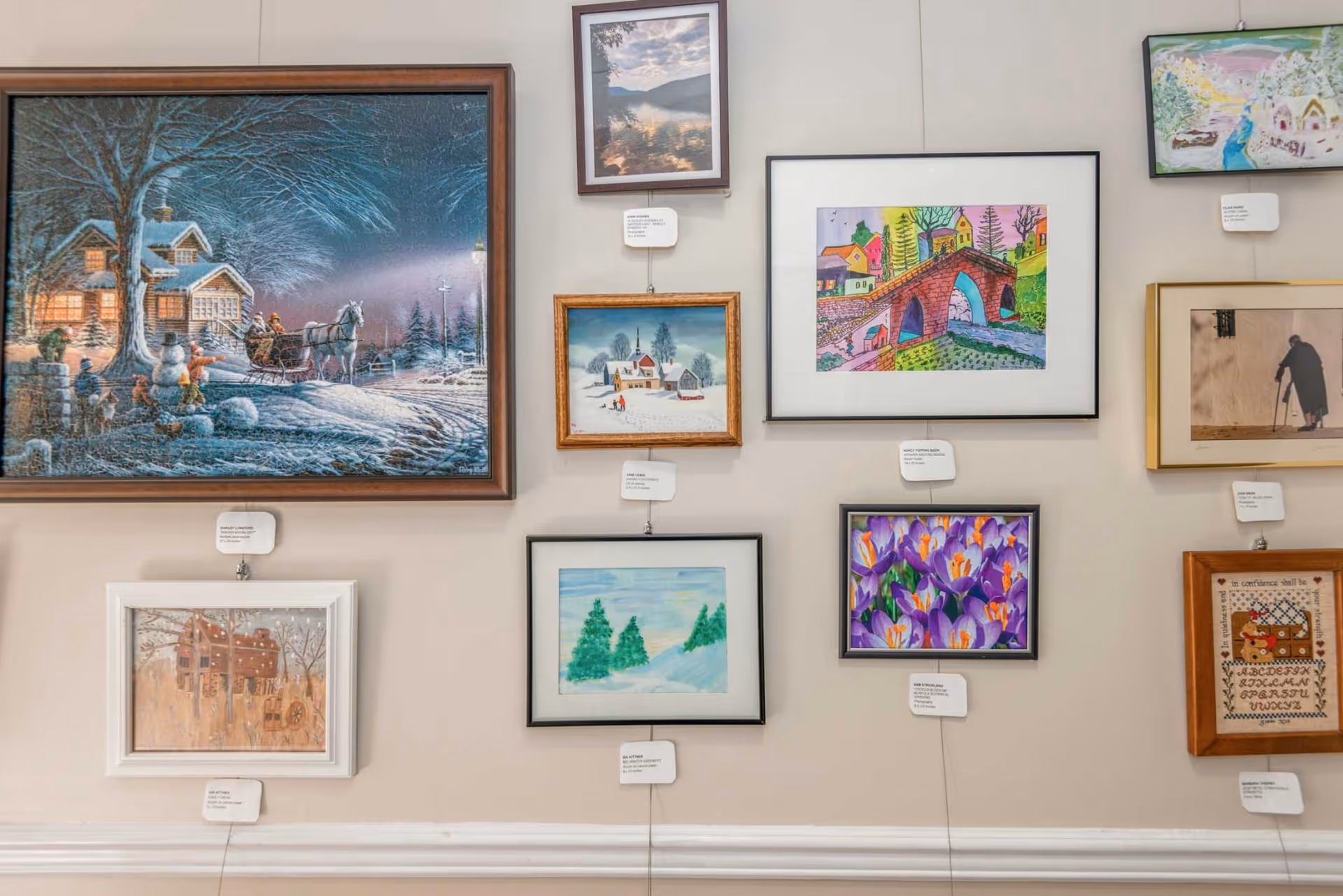 Multiple framed paintings and artwork hung on an interior wall in a gallery-style display.