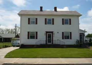 A two-story white building with black shutters, a small front lawn, and a driveway.