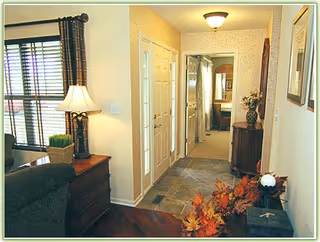A well-lit interior entry hallway with a tiled floor, console tables, a lamp and decorative accents leading into a living area.