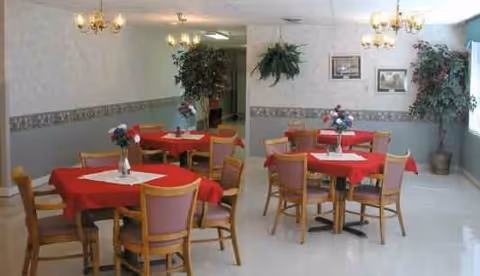 Indoor dining room with red-tablecloth tables, chairs, chandeliers, and potted plants.