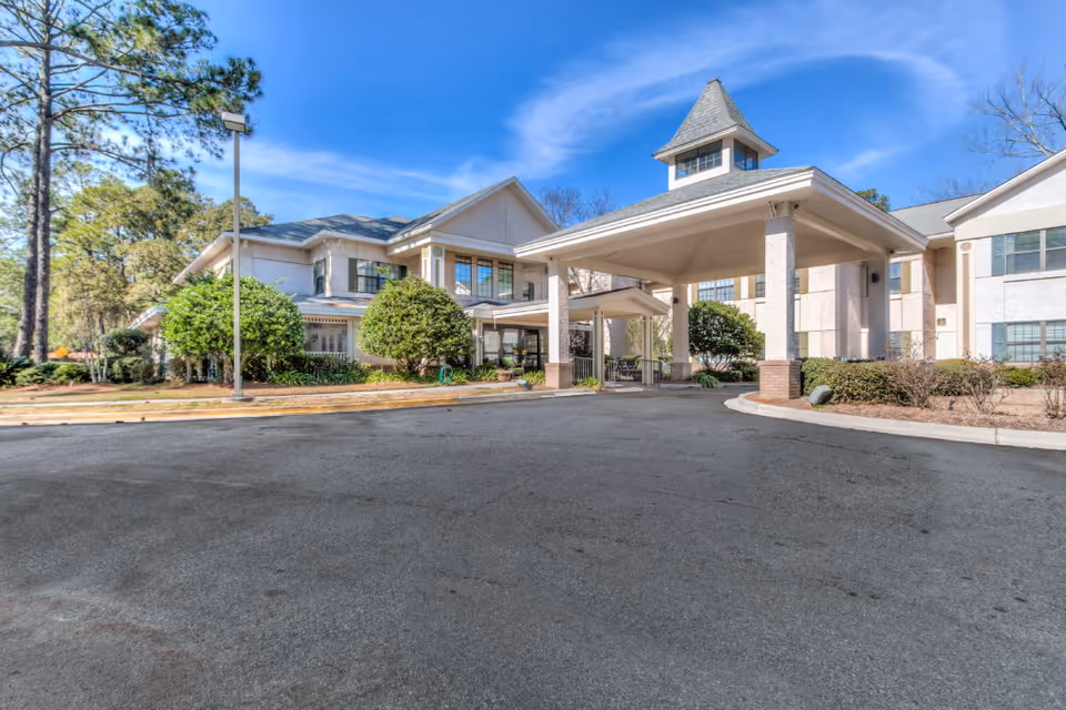 Front entrance of the Oaks at Habersham building with a covered porte-cochere, driveway, and landscaped shrubs under a blue sky.