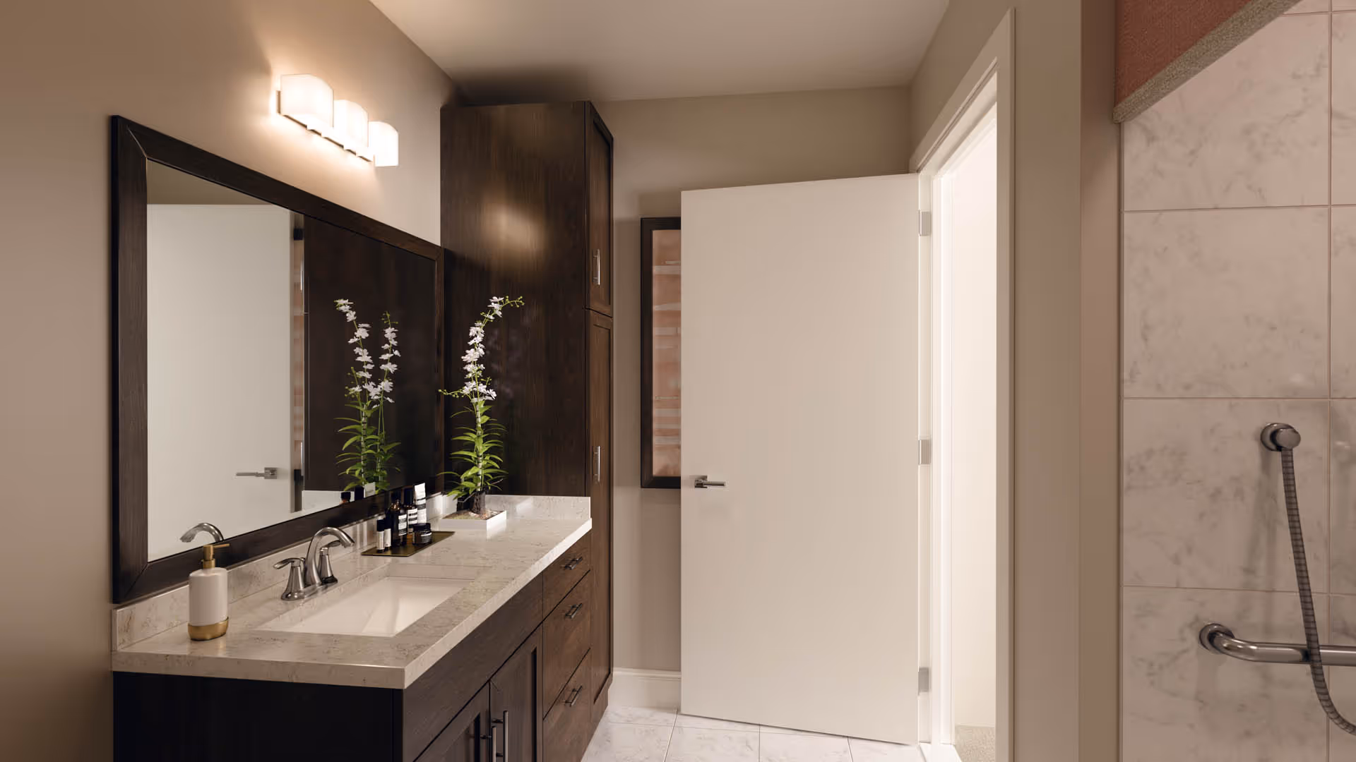Bright modern bathroom with a marble-topped vanity, large mirror, orchids on the counter, and a tiled shower.