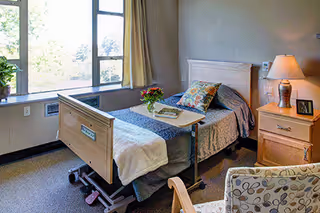 A hospital-style bedroom in a senior living facility with a bed and nightstand.