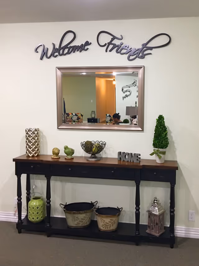 Console table with decorative bowls, plants and a lantern beneath a mirror and a 'Welcome Friends' wall sign.