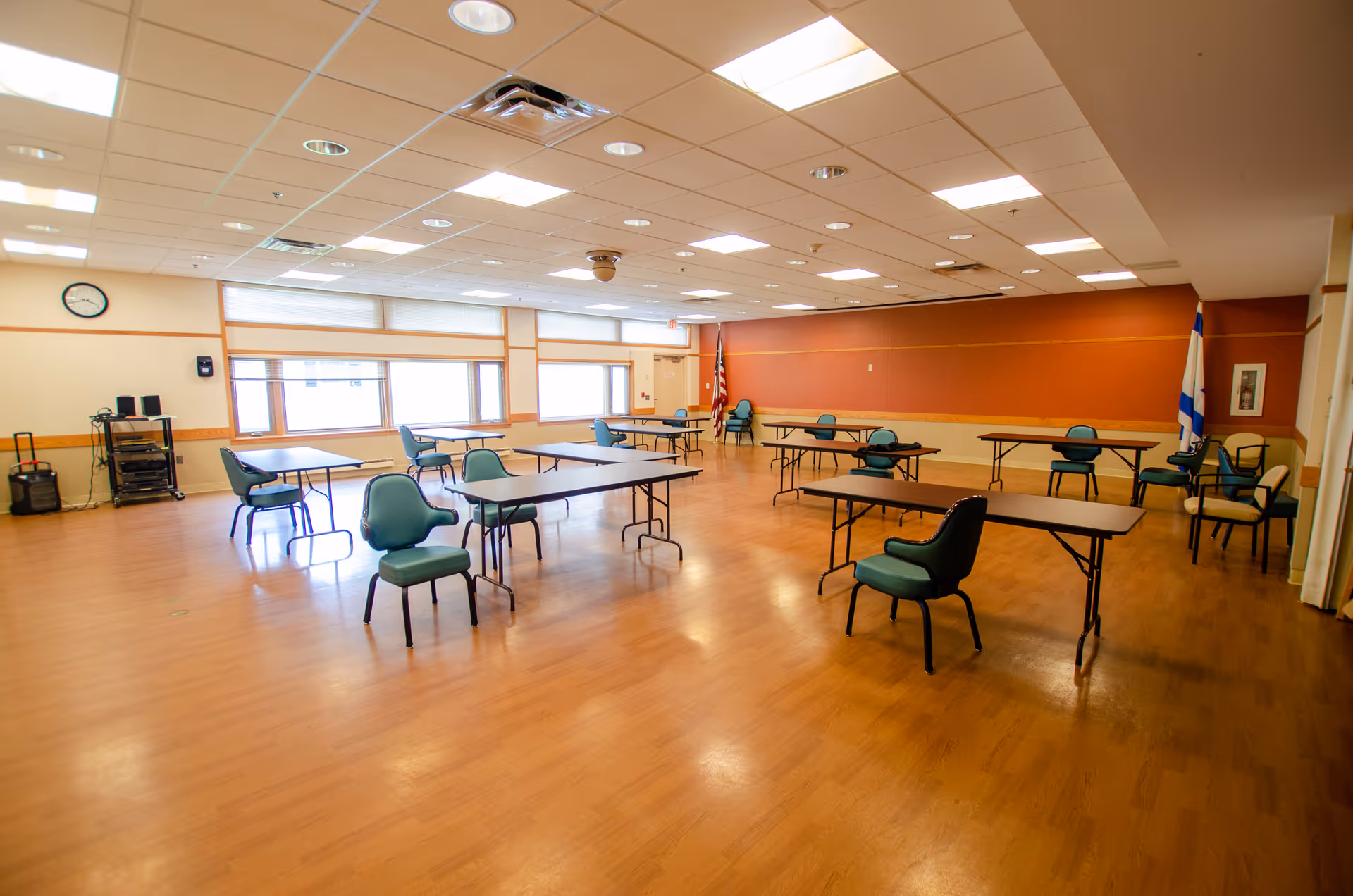 Large multipurpose activity/dining room with scattered tables and green chairs on a wood floor.