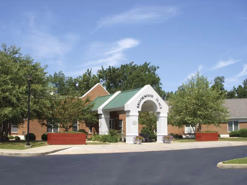 Front view of Brookwood Place senior living facility entrance with trees and landscaping.