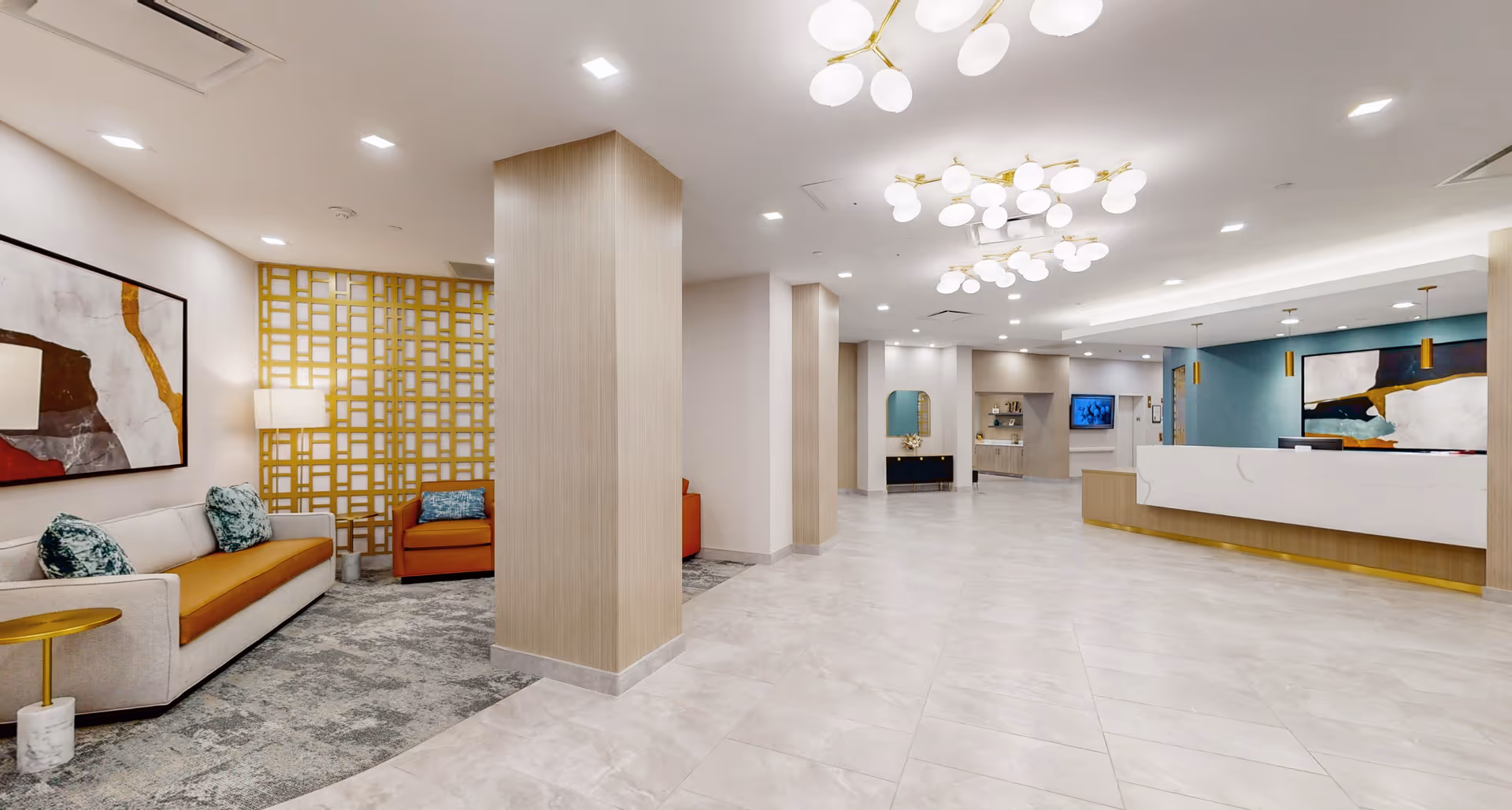 Bright modern lobby with seating areas, decorative lighting fixtures, and a reception desk.
