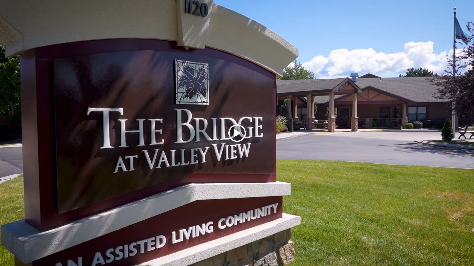 Outdoor view of the entrance area of The Bridge at Valley View assisted living community, featuring a large sign with the community name and a building with a covered entrance in the background.