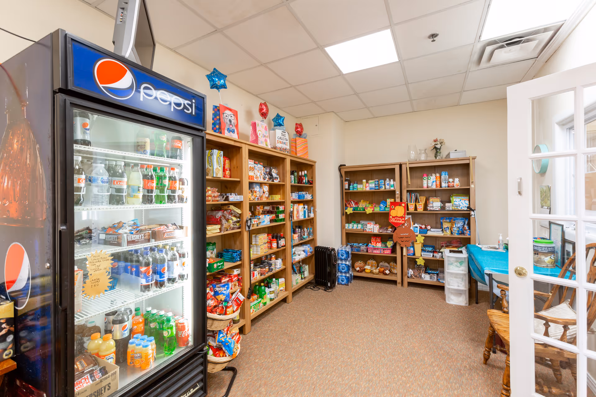 Small on-site convenience shop with a Pepsi refrigerator and shelves stocked with snacks and beverages in a senior living community.