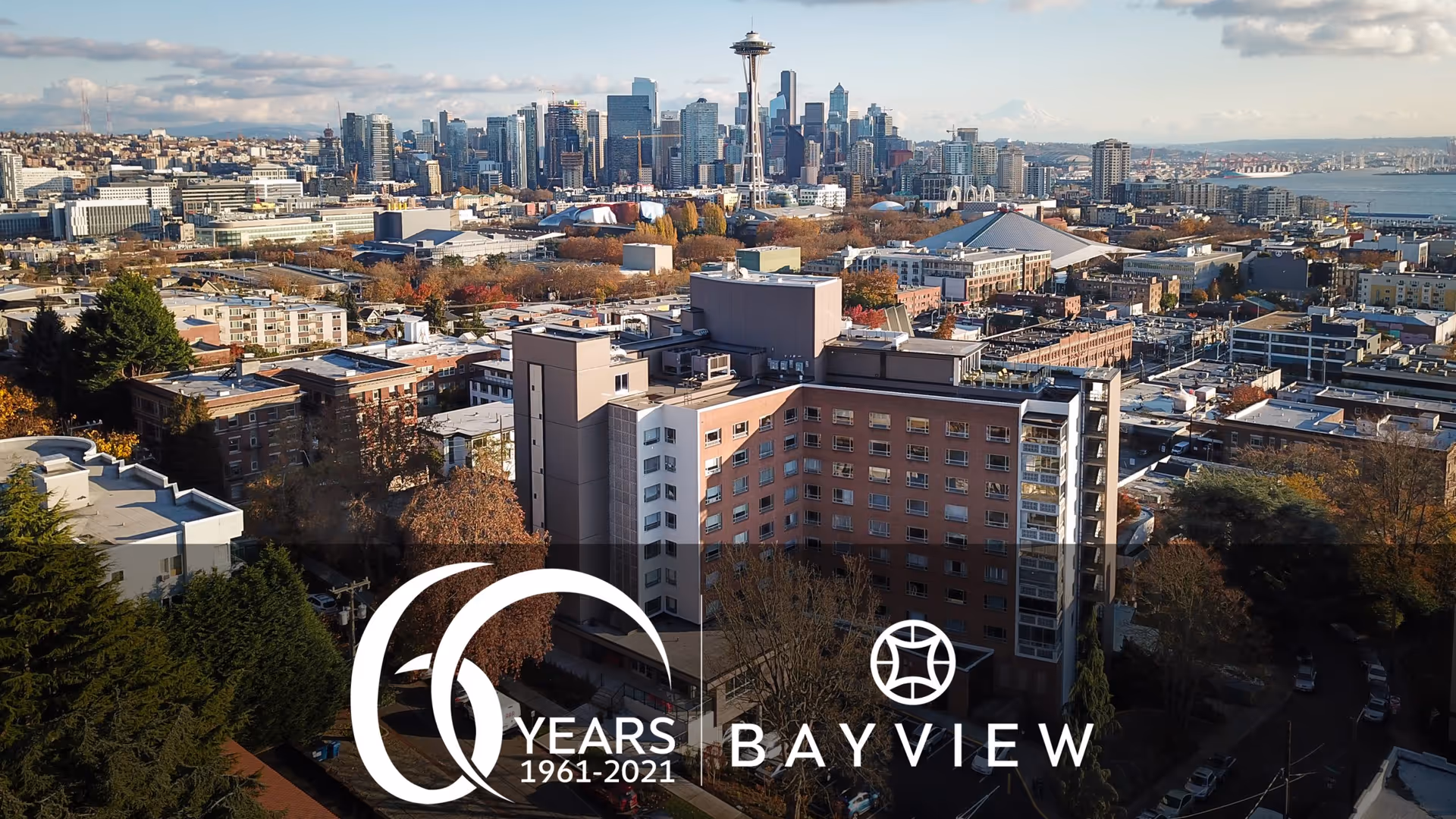 Aerial view of Bayview Retirement Community building with a city skyline in the background under a partly cloudy sky during daytime.