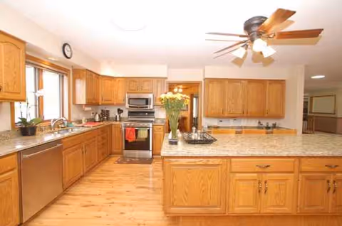 Bright kitchen with island, wooden cabinets, stainless appliances, and a vase of flowers.