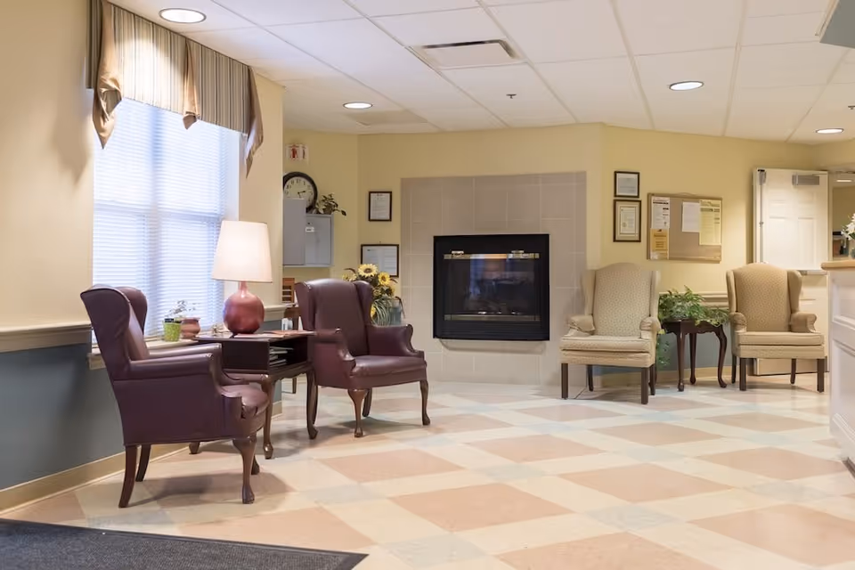 Cozy common sitting area with armchairs, side tables, a lamp and a fireplace in an assisted living facility.