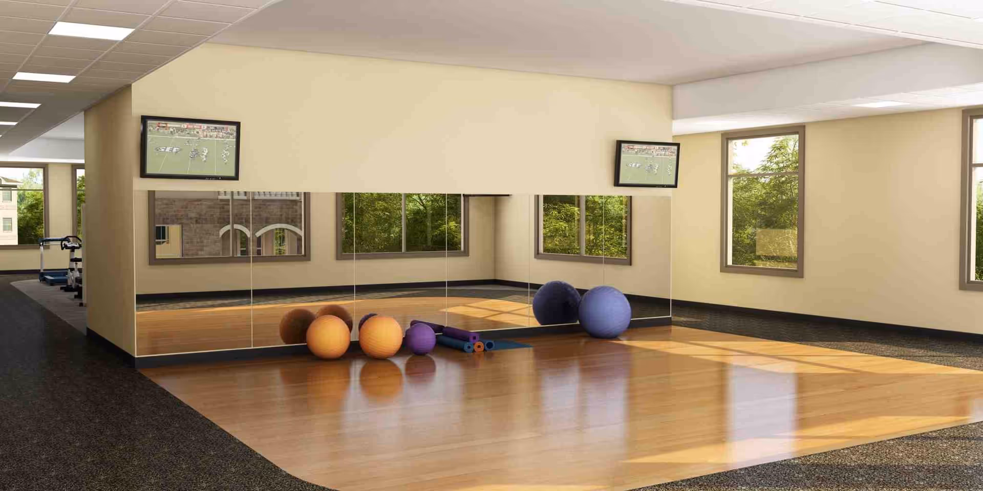 Empty exercise studio with hardwood floor, mirrored wall, exercise balls and mats, and wall-mounted TVs.