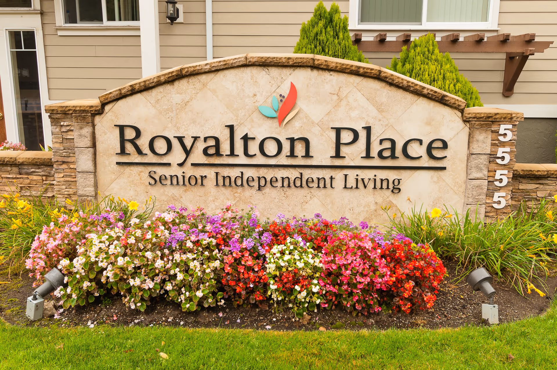 Stone sign for Royalton Place Senior Independent Living with colorful flowers planted in front and a building exterior in the background.