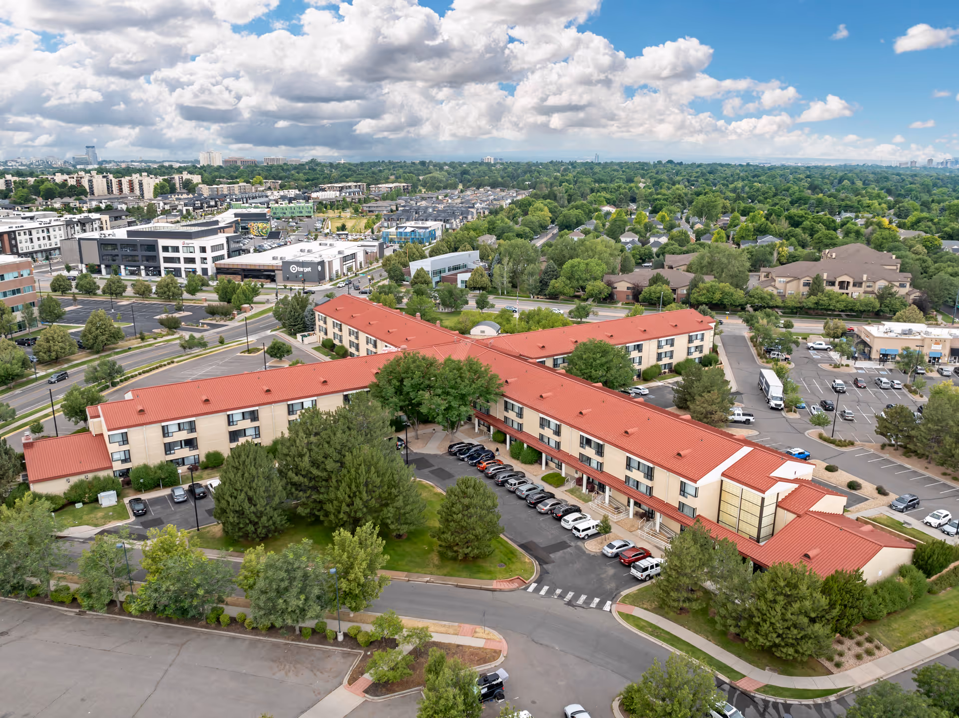 Aerial view of Brookdale Lowry facility with a large building featuring a red roof surrounded by trees and parking lots. The surrounding area includes residential neighborhoods, commercial buildings, and a Target store under a partly cloudy sky.