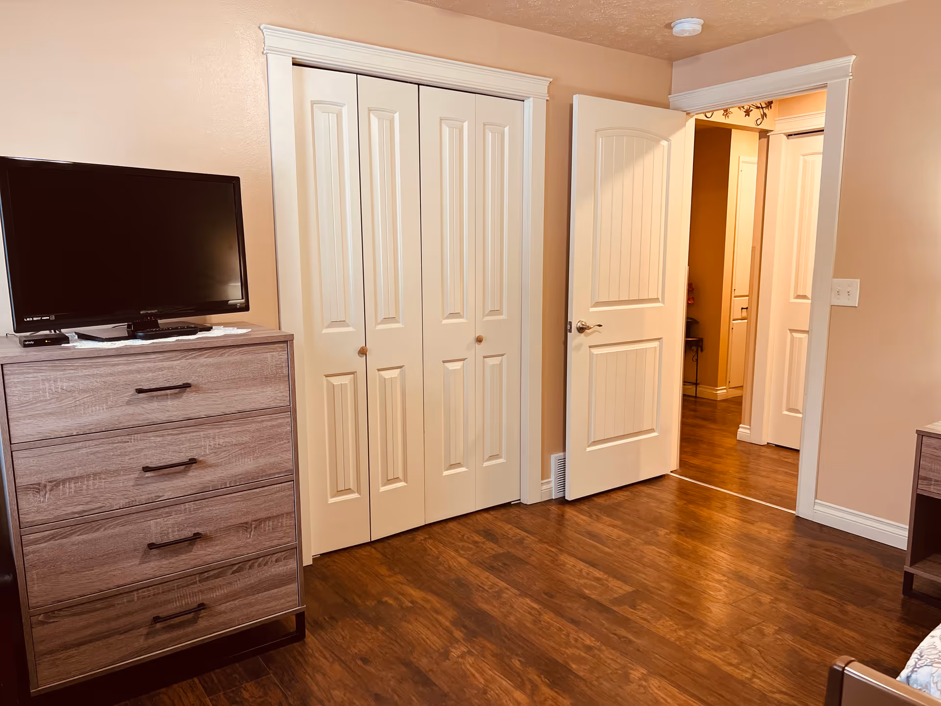 Bedroom interior with a dresser and TV, double closet doors, and an open doorway into a hallway.