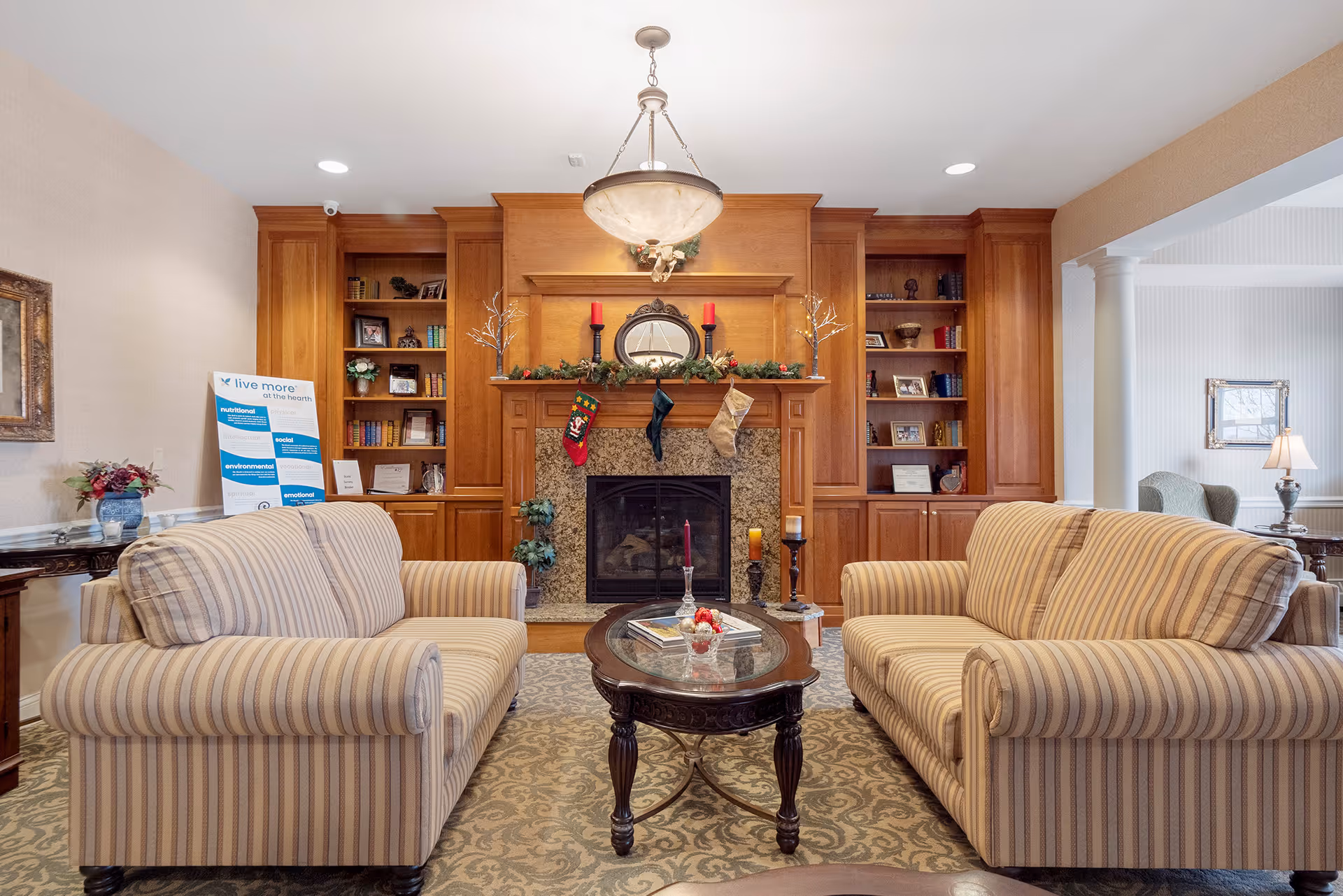 Cozy lounge with two striped sofas facing a fireplace flanked by wooden built-in bookshelves and a central coffee table.