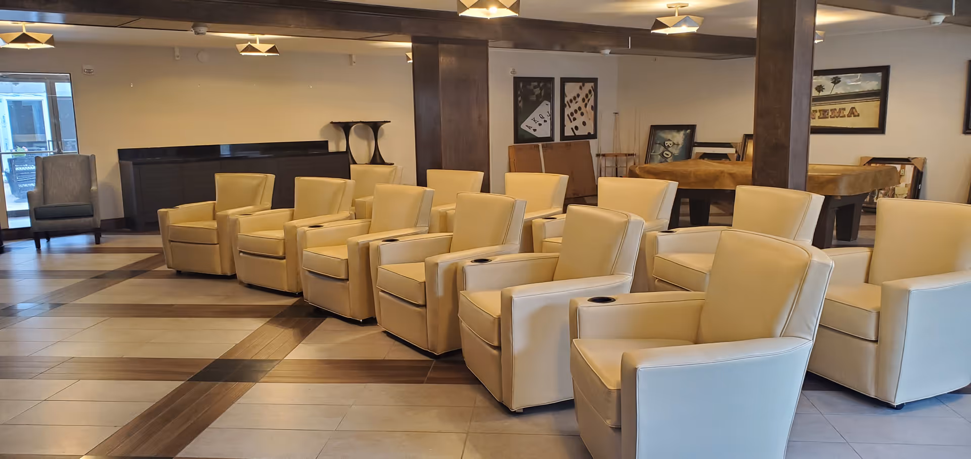 Row of beige recliner chairs arranged in a communal lounge area with tiled floor, wooden columns and game tables in the background.
