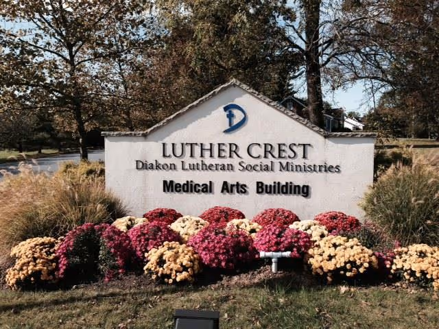 Outdoor sign for Luther Crest Diakon Lutheran Social Ministries Medical Arts Building surrounded by colorful flowers and trees in the background.