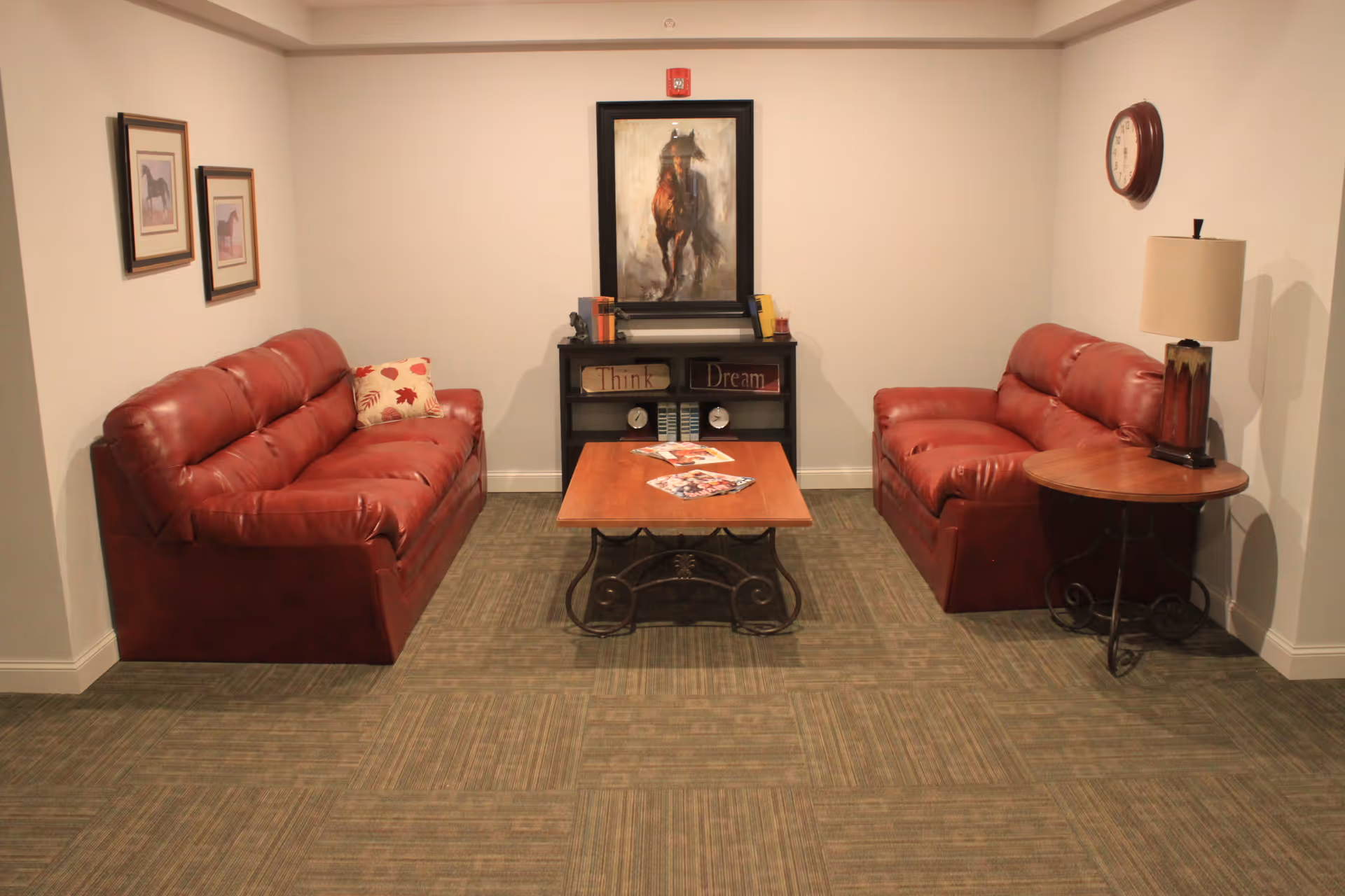 Small sitting room with two red leather sofas facing a coffee table and a framed horse painting on the back wall.