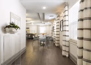 Bright communal dining area with round tables and chairs, striped curtains, and a decorative console with a plant.