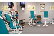 Small interior fitness room with teal-padded exercise machines, free weights and wall-mounted TVs.