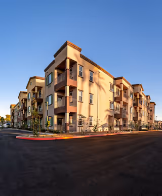 Exterior view of a modern multi-story senior living apartment building with balconies, set against a clear blue sky during daylight.